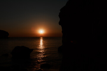 waves wash the rocky shore of the sea. Sunset. Reflection in the water of the bridge and rays