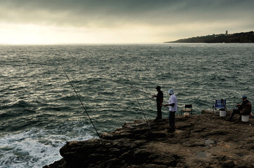 Fototapeta na wymiar three fishermen on the coast in twilight