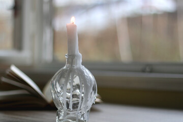 Lit candle in the candle holder and open book on a table. Dark academia concept. Selective focus.