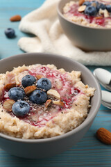 Tasty oatmeal porridge with toppings on light blue wooden table, closeup