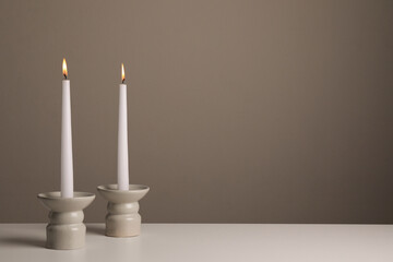 Holders with burning candles on white table near pale brown wall, space for text