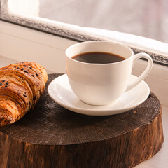 A cozy concept. Classic winter breakfast. A cup of coffee and a croissant stand on the windowsill.