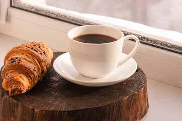 A cozy concept. Classic winter breakfast. A cup of coffee and a croissant stand on the windowsill.