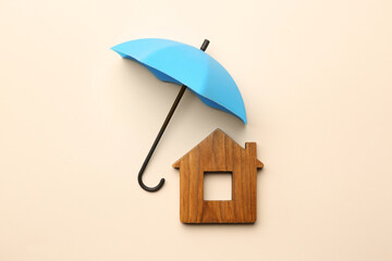Mini umbrella and house model on beige background, flat lay