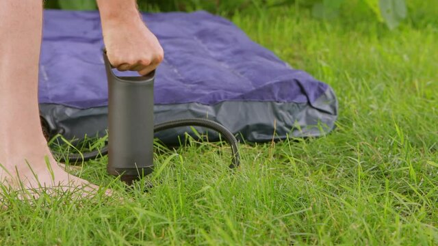 Man inflates air mattress with hand pump outdoors