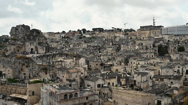 Matera, Basilicata, Italy. August 2021. Amazing pan footage that starts from the historic houses called the stones and ends on the left on the Rock Church of Santa Maria di Idris. People in the alleys
