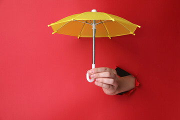 Woman holding open small yellow umbrella through hole in red paper, closeup - obrazy, fototapety, plakaty