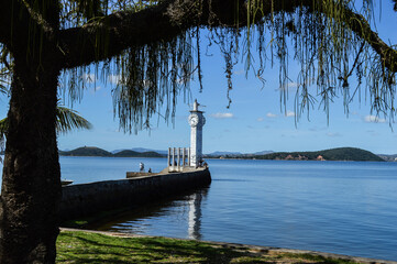 Paisagem na praia onde possui um pier com farol na ponta
