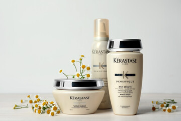 MYKOLAIV, UKRAINE - SEPTEMBER 07, 2021: Set of Kerastase hair care cosmetic products and chamomile flowers on white wooden table