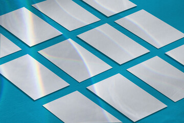 Many empty white horizontal rectangle a4 poster, business card or flyer mockups lying diagonally with overlay of rainbow light refraction caustic effect on blue concrete background. Isometric view