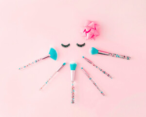 Creative concept of a woman's face with make-up brushes and artificial eyelashes. Minimal makeup background.