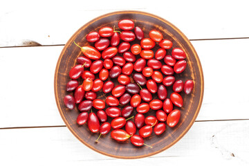 Several bright red ripe dogwood berries on a clay plate on a wooden table, close-up, top view.