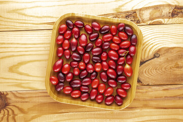 Several bright red ripe dogwood berries on a bamboo plate on a wooden table, close-up, top view.