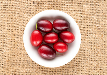 Several bright red ripe dogwood berries on a ceramic white saucer on sacking, close-up, top view.