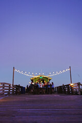 Blurred background of people at a tiki bar on a beach pier at sunset