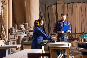 Young female apprentice polishing wood under senior colleague supervision
