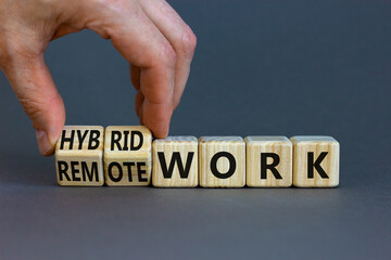 Hybrid or remote work symbol. Businessman turns cubes and changes words 'remote work' to 'hybrid work'. Beautiful grey background. Business, hybrid or remote working concept, copy space.