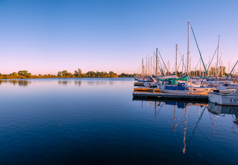 Obraz premium A row of boats sits idle in a harbour in Lake Ontario during sunset, reflecting in the still water.