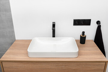 A modern sink in the bathroom with a matte black tap, wall lined with gray ceramic tiles.