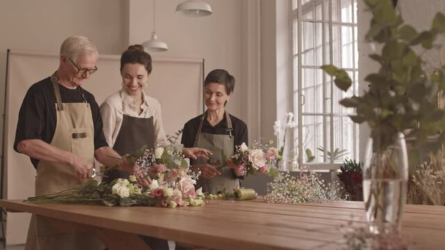 Medium shot of young professional female florist helping kind adult couple with flower arrangement during floral masterclass in cozy flower studio
