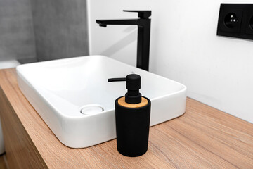 Fototapeta premium A modern washbasin in the bathroom in a wall mounted cupboard with a matte black faucet, a wall lined with gray ceramic tiles.