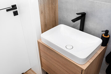 A modern washbasin in the toilet in a wall mounted cupboard with a matte black faucet, a wall lined...