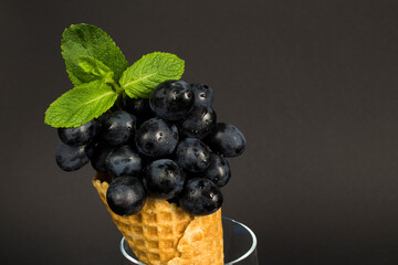 Close-up on black grapes in the ice cream cone on the dark background. Copy space.
