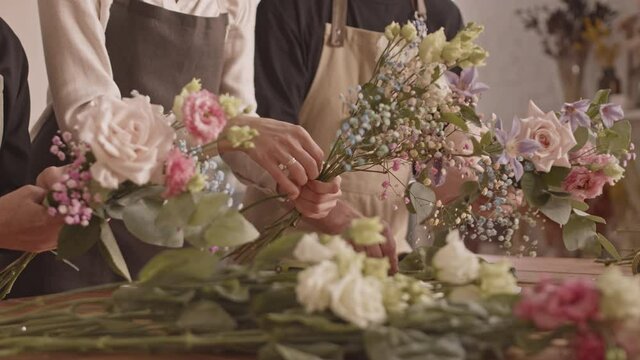 Midsection shot of unrecognizable florists in aprons arranging beautiful flowers in bouquets working together in small flower shop