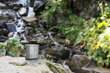 Cup on rock near mountain waterfall. Space for text