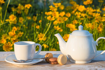 Summer tea time or coffee break; white teapot and white cup of tea or coffee, french macaroons on...