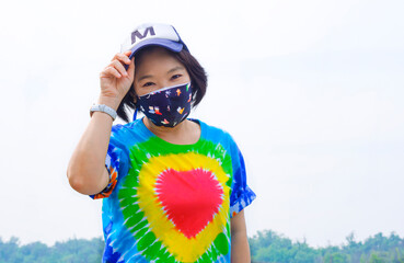 Plus size LGBT woman in rainbow t shirt with cap and fabric face mask looking at camera in confident expression on lacking sky background