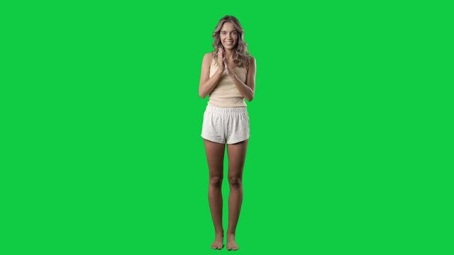 Cute woman in sleepwear applauding and clapping looking at camera. Full body on green screen chroma key background