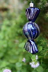 Blue candy Christmas toy on a fir tree. Green background with copy space. Christmas decorations close up photo. 