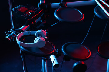 Modern electronic drum kit with headphones on dark background, color toned. Musical instrument