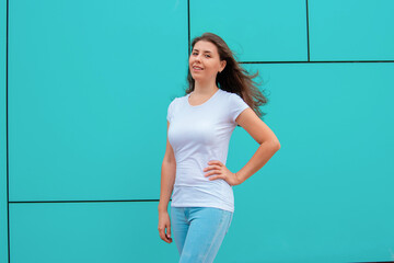 Attractive girl in white T-shirt posing against the backdrop of a turquoise wall. Mock-up.