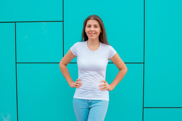 Attractive girl in white T-shirt posing against the backdrop of a turquoise wall. Mock-up.