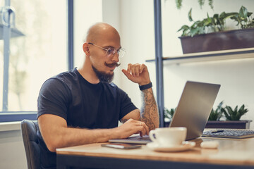 Bolded man with mustache and beard works on computer at home office, programmer, writer, freeelancer.