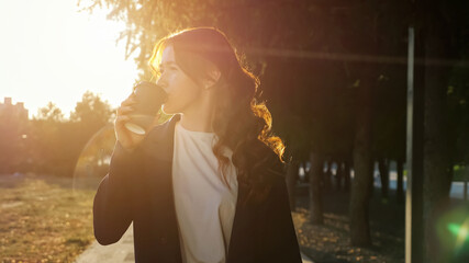 Young woman with flecks on face and copper hair talks on contemporary cellphone above street of large city at sunset light close view