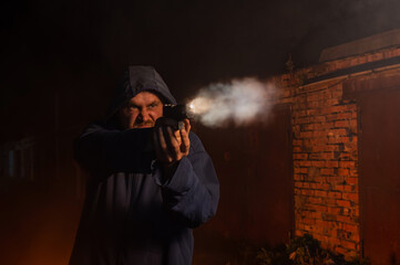 Caucasian man in a hood shoots a pistol.