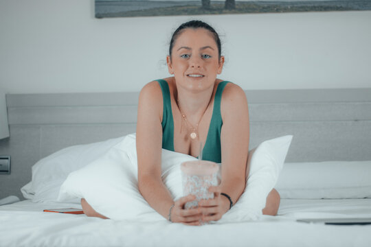 Muchacha joven empresarial formal desayunando t&eacute; con la almohada sentada en la cama de la habitaci&oacute;n