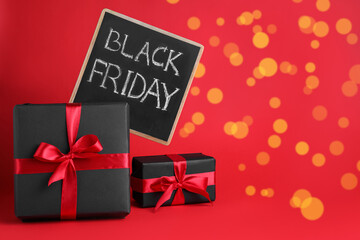 Gift boxes and chalkboard with words Black Friday on red background, space for text