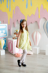 A girl in a yellow dress with black polka dots poses in a photo studio.