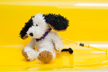 Pediatric vaccination concept. Soft toy dog with syringe in left upper arm on yellow background