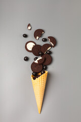 Waffle ice cream cone with chocolate chip cookies stuffed with chocolate dragees on gray background