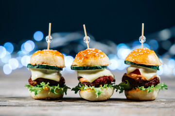 Close up of mini burgers with cheese, onion, lettuce salad and cucumber, isolated on wood background. Party snacks, fast food concept
