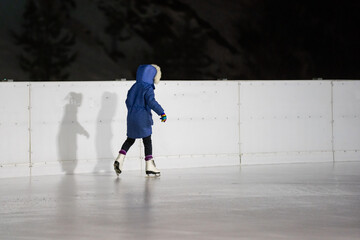 Cute little girl ice skating on a rink in the city center
