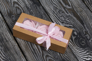 Homemade marshmallows in craft packaging. Zephyr in the form of a rose. Against the background of pine boards.