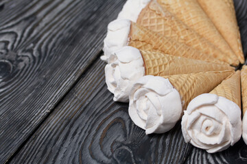 Homemade marshmallows are spread out on the table surface. Zephyr in a waffle cone. Made in the shape of a rose. Close-up shot.