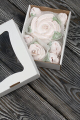 Homemade marshmallows in craft packaging. Zephyr in the form of a rose. Against the background of pine boards.