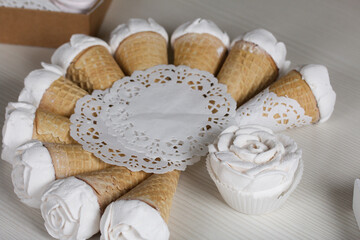 Homemade marshmallows are spread out on the table surface. Zephyr in a waffle cone. Made in the shape of a rose. Close-up shot.